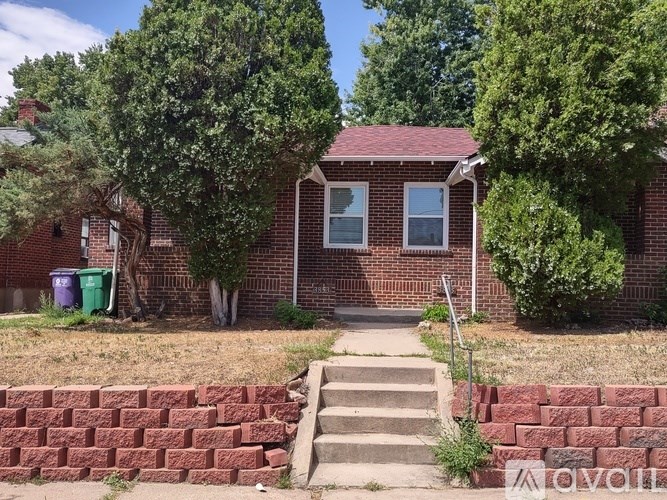 A red brick house with a green trash can and a grey metal railing.