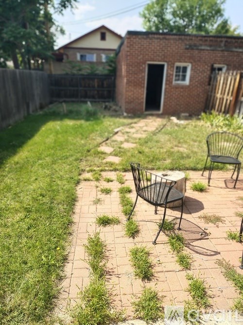 A backyard with a brick patio and a small brick building in the background.