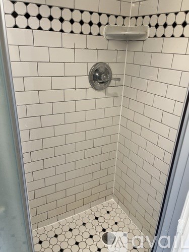 A white tiled shower with a silver faucet.