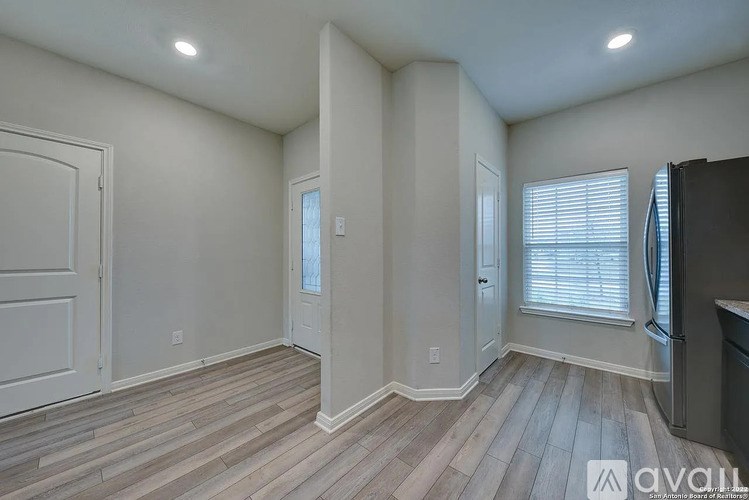 A room with wood flooring and white walls, with a door on the left and a window with blinds on the right.
