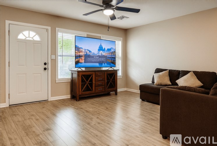 A living room with a brown couch, a flat screen TV, and a ceiling fan.