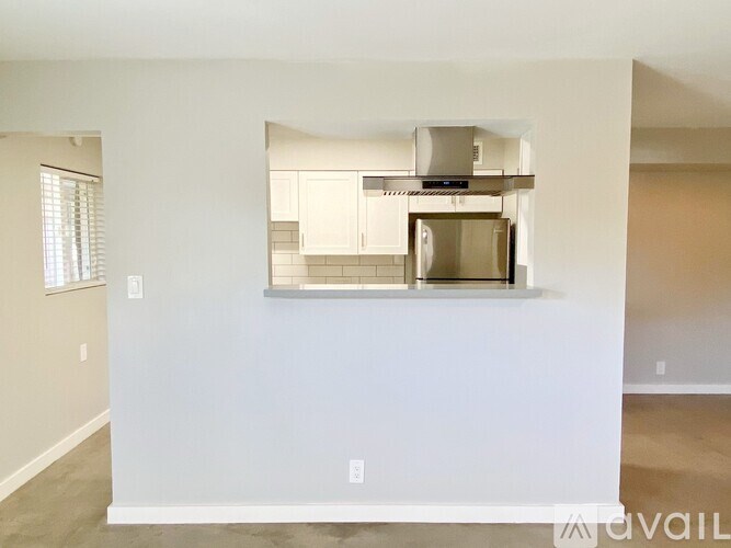 A kitchen with white cabinets and a stainless steel refrigerator is visible through a window.