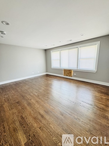 A room with wooden flooring and two windows.