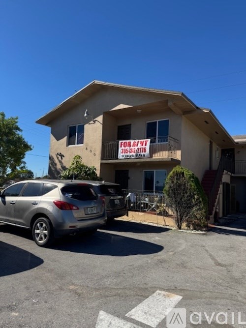 A house with a car parked in front and a for sale sign on the balcony.