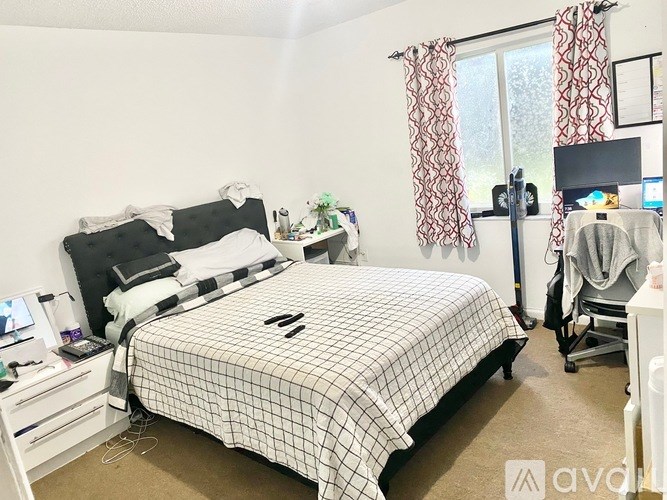 A bedroom with a bed, nightstand, and window with curtains.