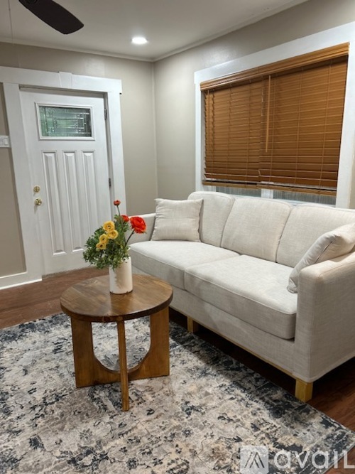 A living room with a white couch, a round wooden table with a vase of flowers on it, and a rug on the floor.