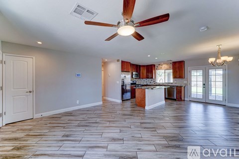 A spacious room with a ceiling fan and a kitchen area in the background.