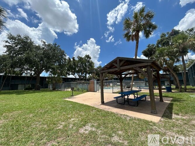A pavilion with a bench is situated in a grassy area with trees in the background.