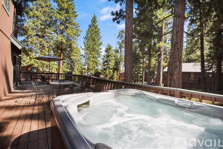 A hot tub sits on a wooden deck with trees in the background.