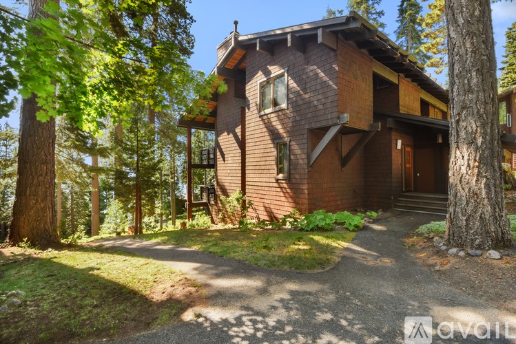 A brown wooden house with a porch and a tree in front.