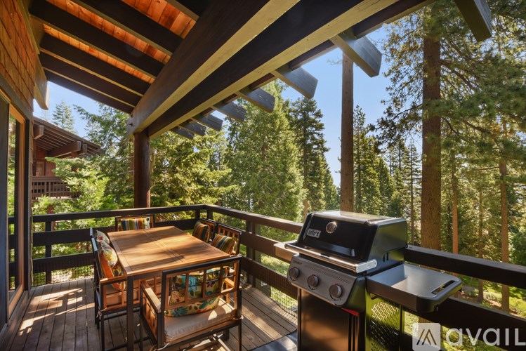 A wooden deck with a grill and chairs overlooking a forest.