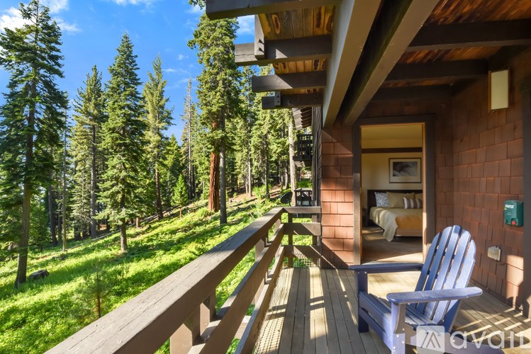 A wooden deck with a blue chair and a bedroom inside a cabin.