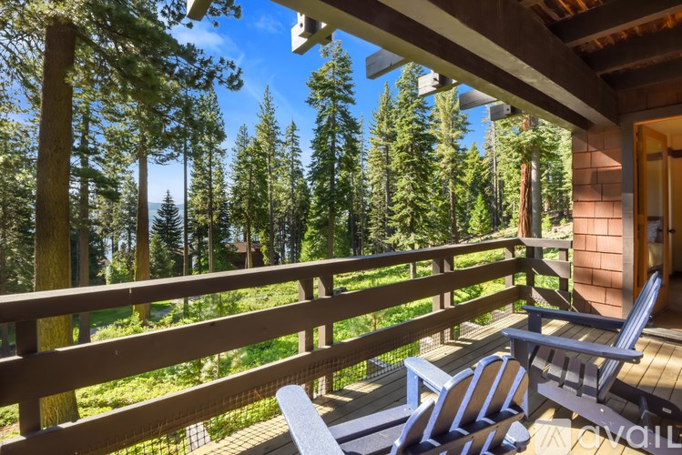A wooden deck with two chairs and a table is overlooking a forest.