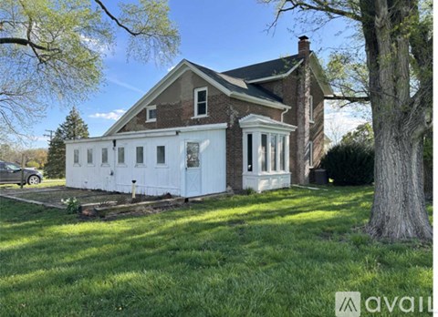 A house with a white exterior and a brick chimney is surrounded by a grassy lawn and trees.