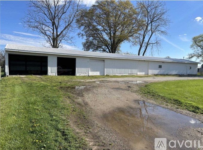 A large white building with a metal roof and a dirt path leading to it.
