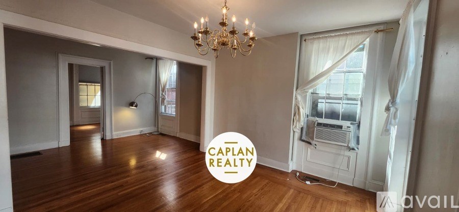 A spacious room with wooden floors and a chandelier is available for rent.