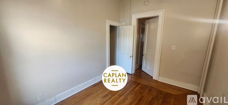 A room with wooden floors and white walls, with a doorway leading to another room.