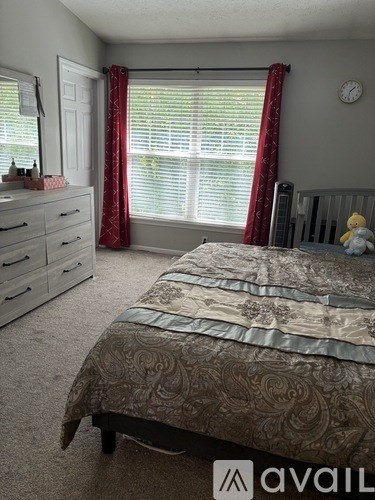 A bedroom with a bed, dresser, and window with red curtains.