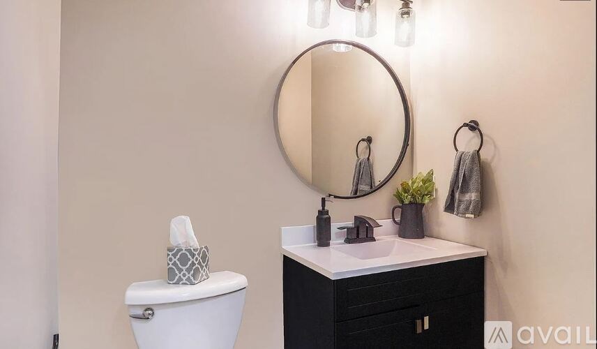 A bathroom with a white toilet, a round mirror, and a sink with a black cabinet.