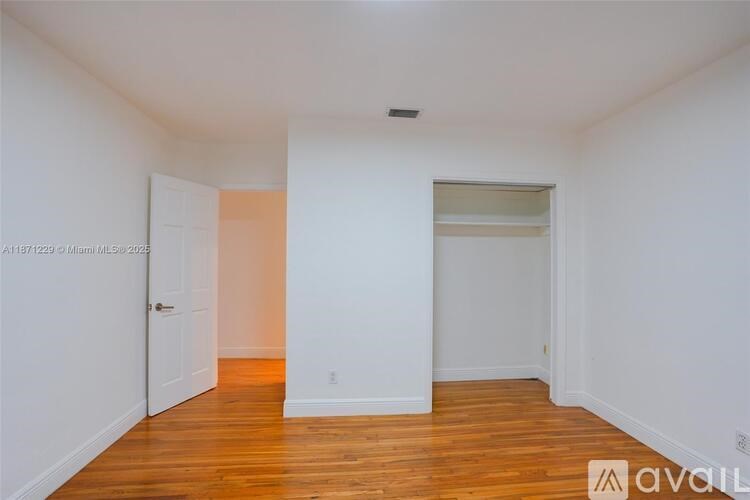 A room with wooden floors and white walls, with a door on the left and a window on the right.