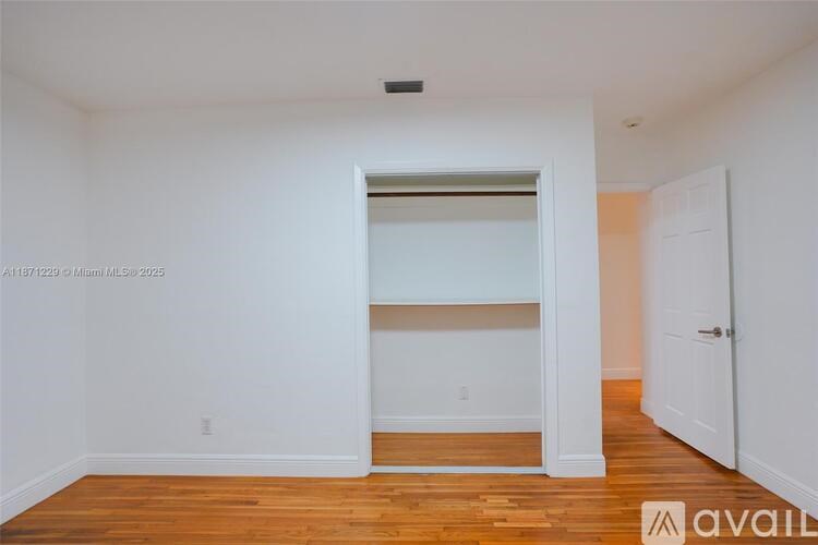 A room with white walls and wooden flooring, with a door on the right and a window on the left.
