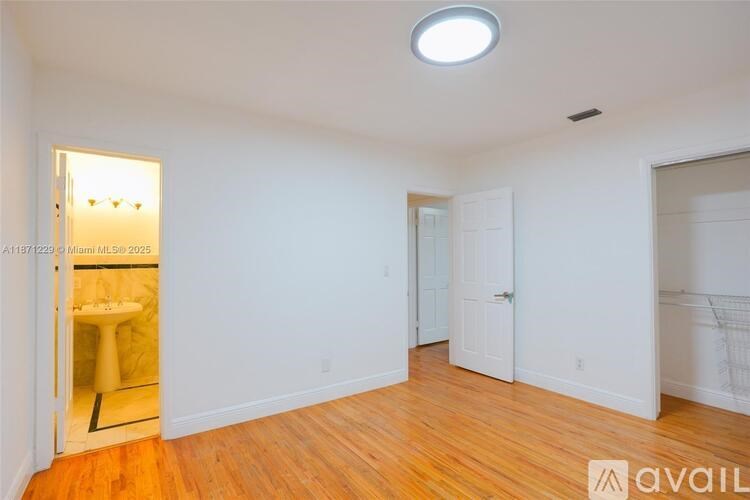 A room with white walls and wooden flooring, with a doorway leading to another room.