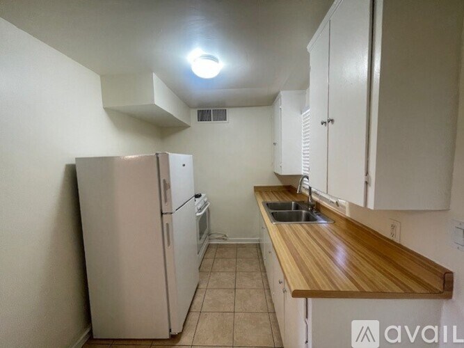 A kitchen with a white refrigerator, wooden countertop, and white cabinets.