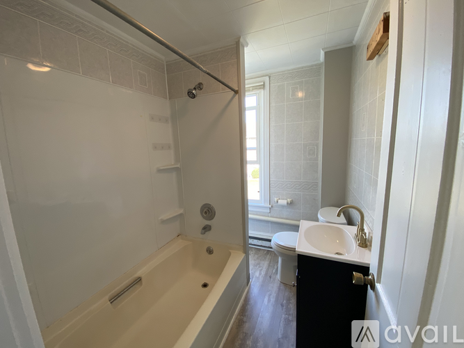 A room with a white door and a brown floor with sunlight coming through the window.