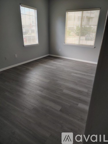 A room with wooden flooring and two windows with blinds.