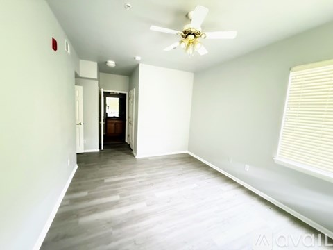 A room with a ceiling fan and light fixture, wooden flooring, and white walls.