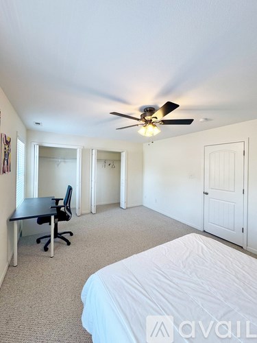 A room with a bed, desk, and ceiling fan.