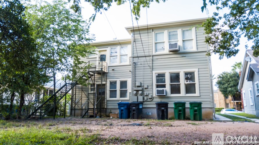 A two-story house with a grey exterior and a green trash can in front.