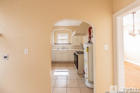 A kitchen with a refrigerator, sink, and cabinets is visible through an archway.