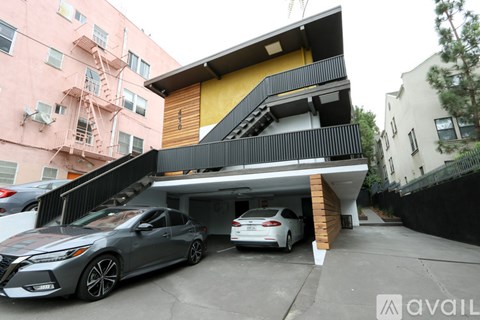 Two cars are parked in a garage attached to a two-story building.