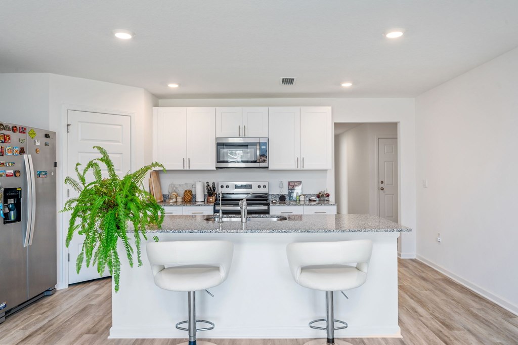 A kitchen with white cabinets and a white island with two stools.