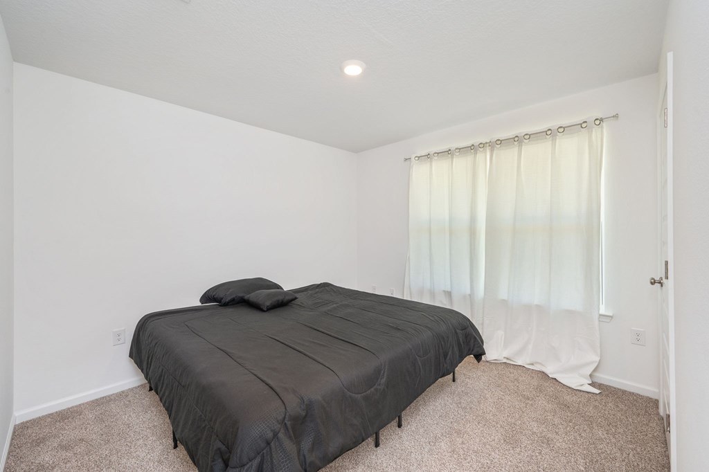 A bedroom with a bed, carpet, and a window with curtains.