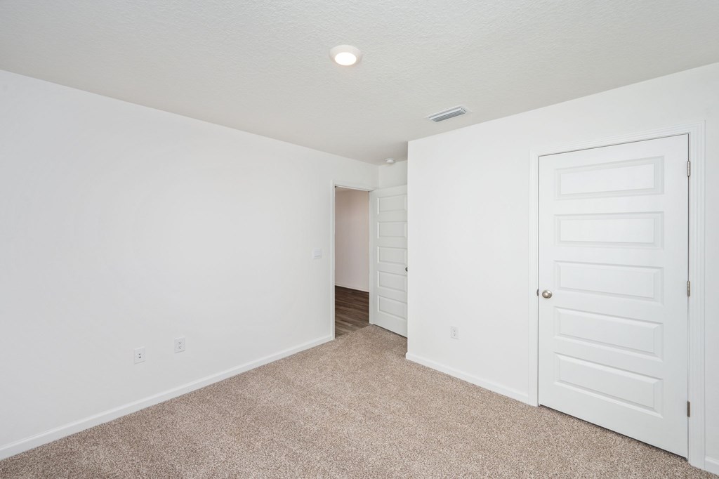 A white door is on the right side of a room with a carpeted floor.