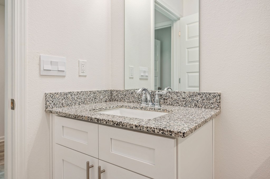 A bathroom sink with a granite countertop and a mirror above it.