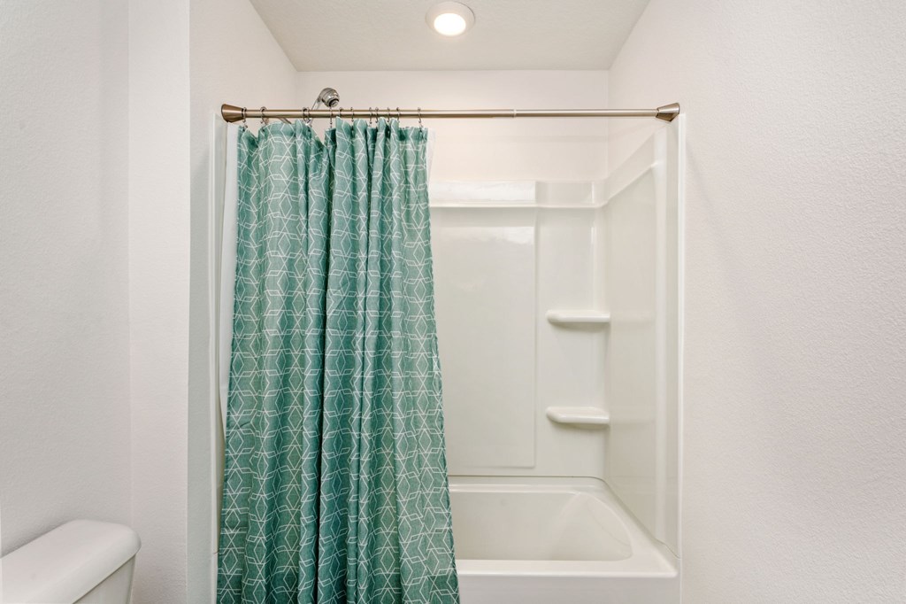 A white bathroom with a green shower curtain.