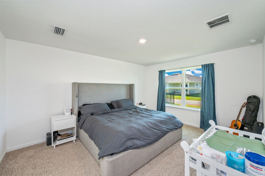 A bedroom with a large bed and a window with a view of a house and trees outside.