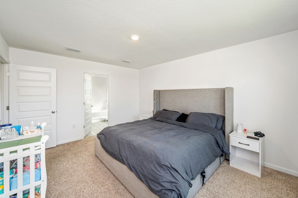 A bedroom with a bed, nightstand, and a baby's crib.
