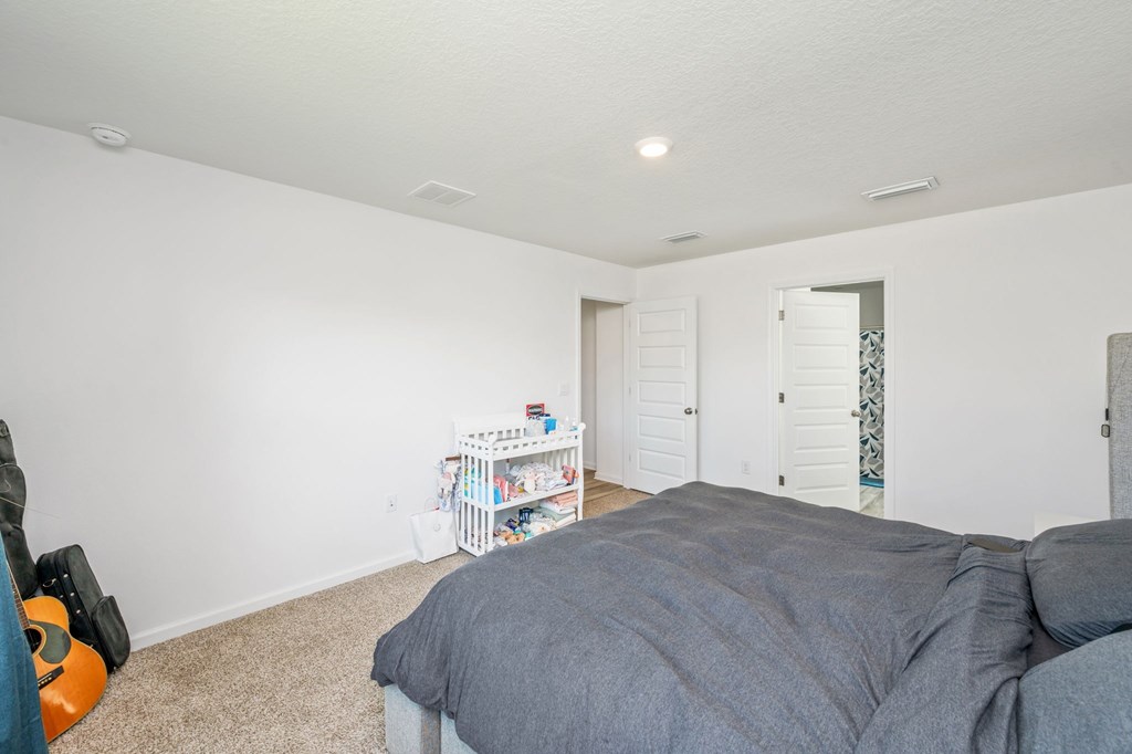A bedroom with a bed, a small table with books, and a wall-mounted shelf.