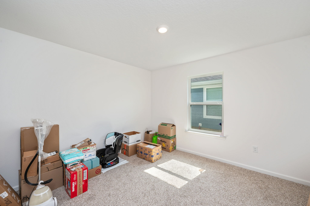 A room with white walls and a window is filled with boxes and packing materials.
