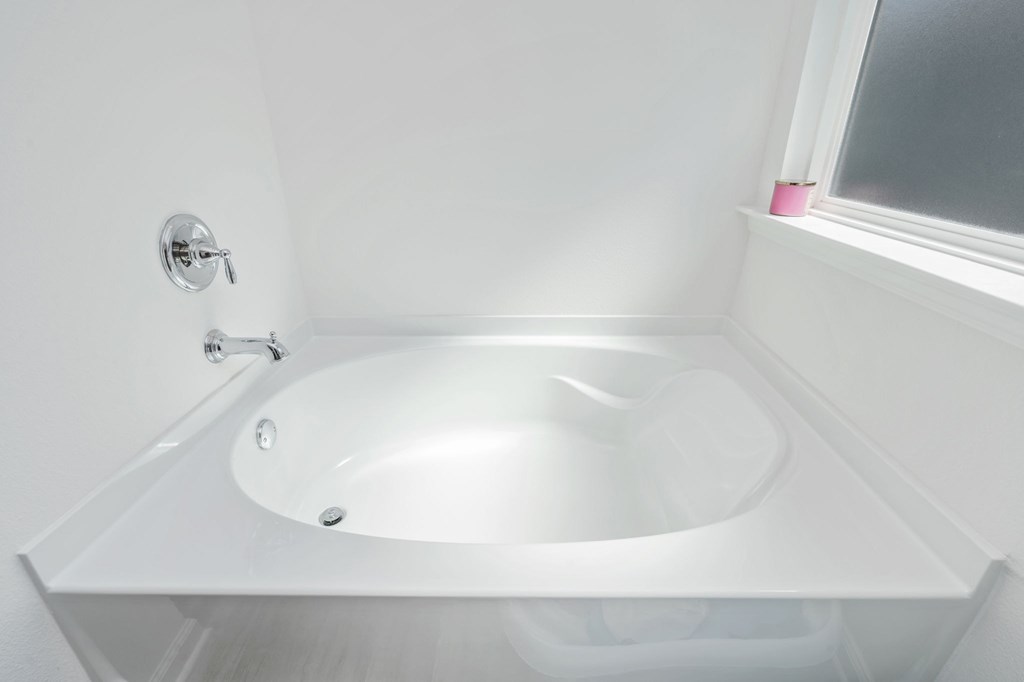 A white bathroom with a white tub and a window.