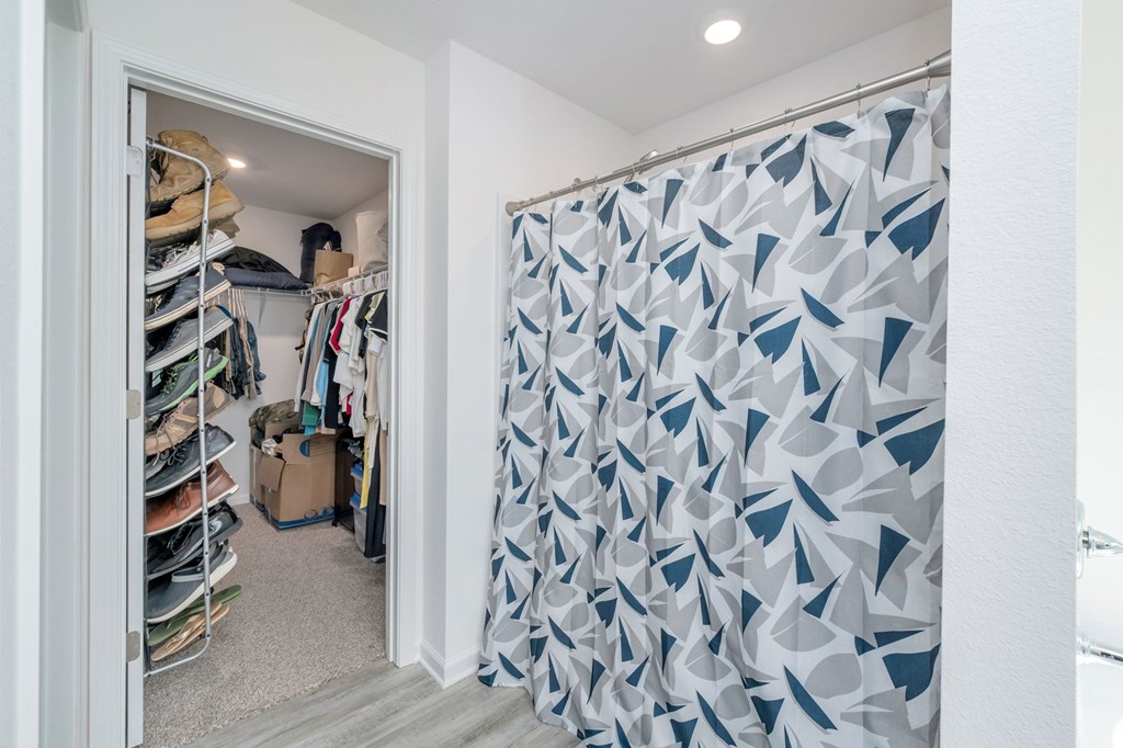 A room with a closet full of clothes and a shower curtain with a geometric pattern.