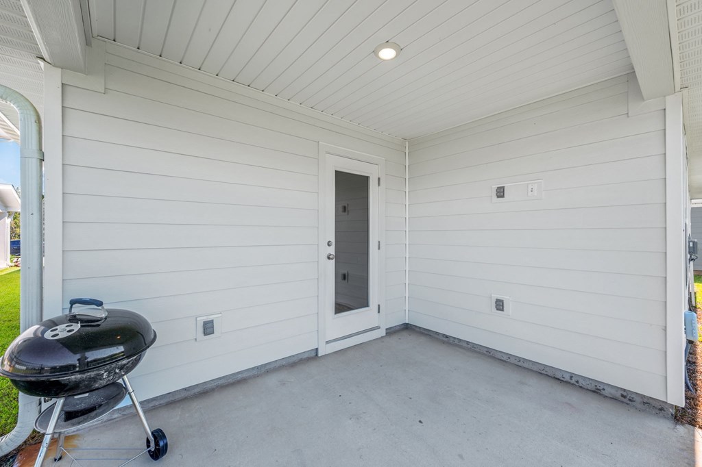 A white covered porch with a grill and a door.