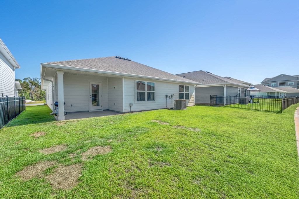 A white house with a brown roof is surrounded by a green lawn and a black fence.