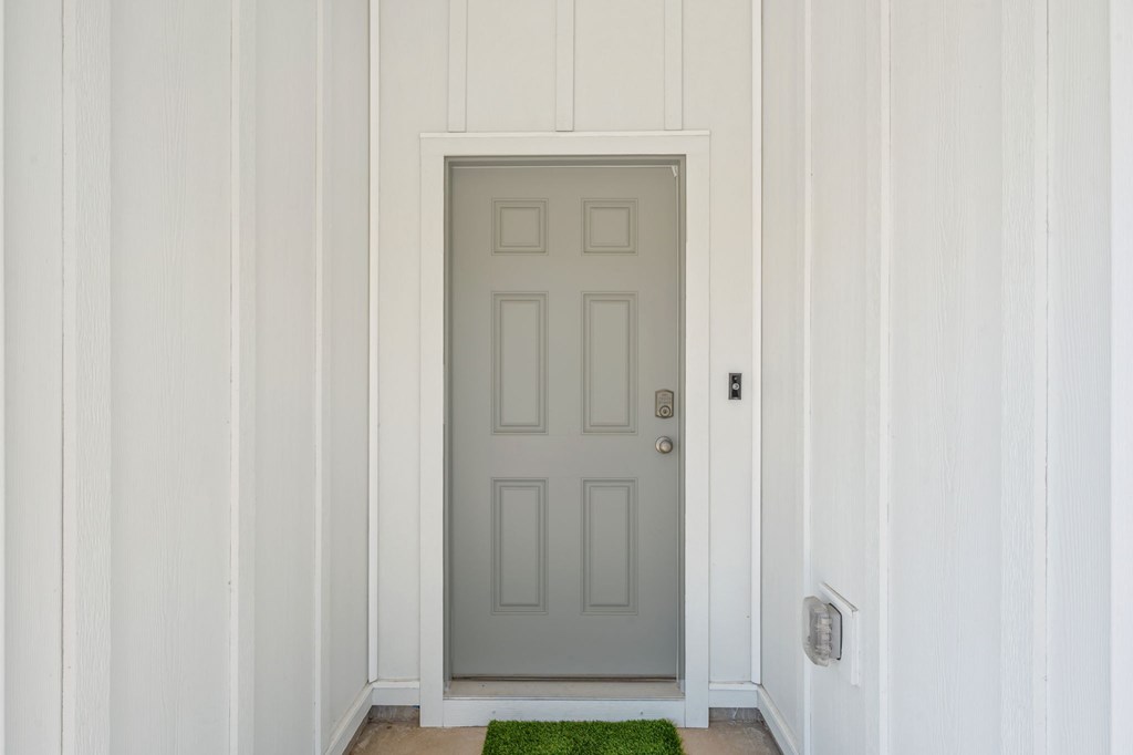 A grey door with a mat in front of it.