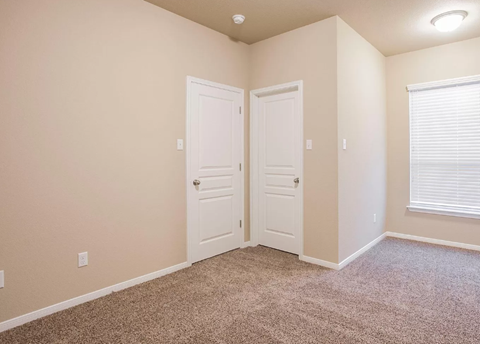 A room with two white doors and a window with blinds.