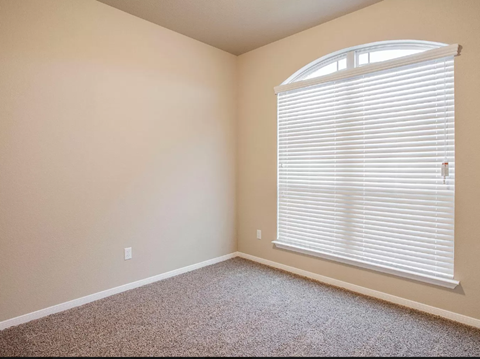 A room with a carpeted floor and a window with blinds.